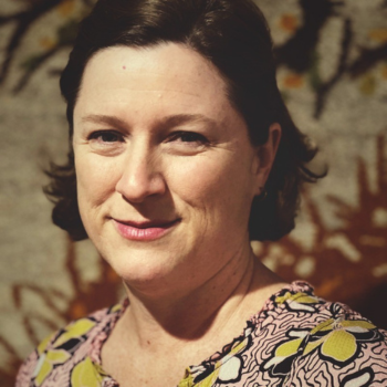 A woman smiling softly in front of a warm-toned floral background.